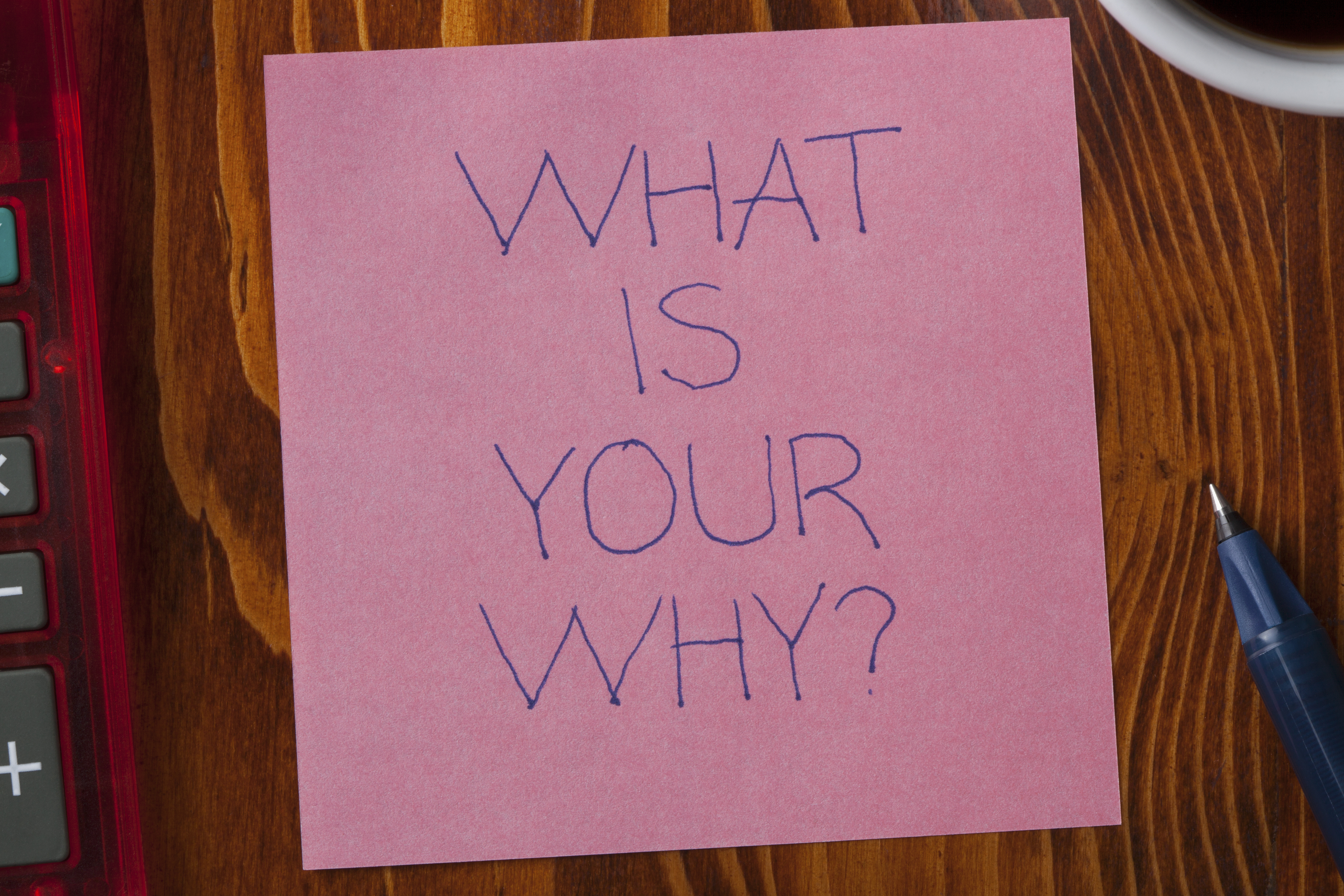 What is your why written on a note on wooden background with pen.